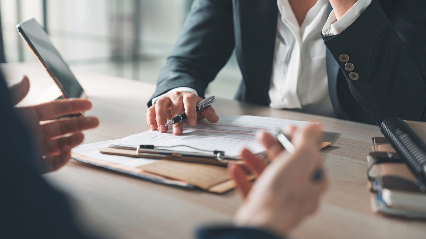 Business owner sitting at a table with an insurance agent carefully reviewing and corporate cyber insurance policy requirements.
