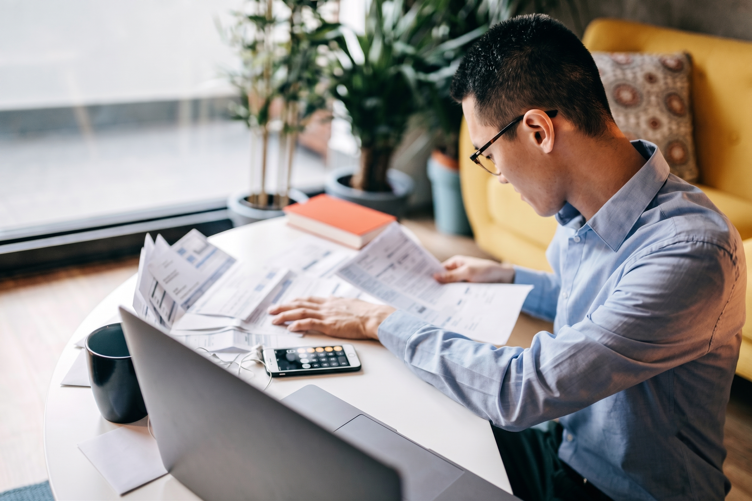 A business professional with glasses sitting at a desk, reviewing paper billing statements to prepare for the financial impact of senate bill 122.